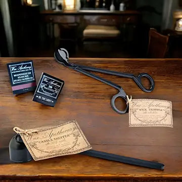 a wick trimmer, candle snuffer, and matchbooks sitting on a wooden desk