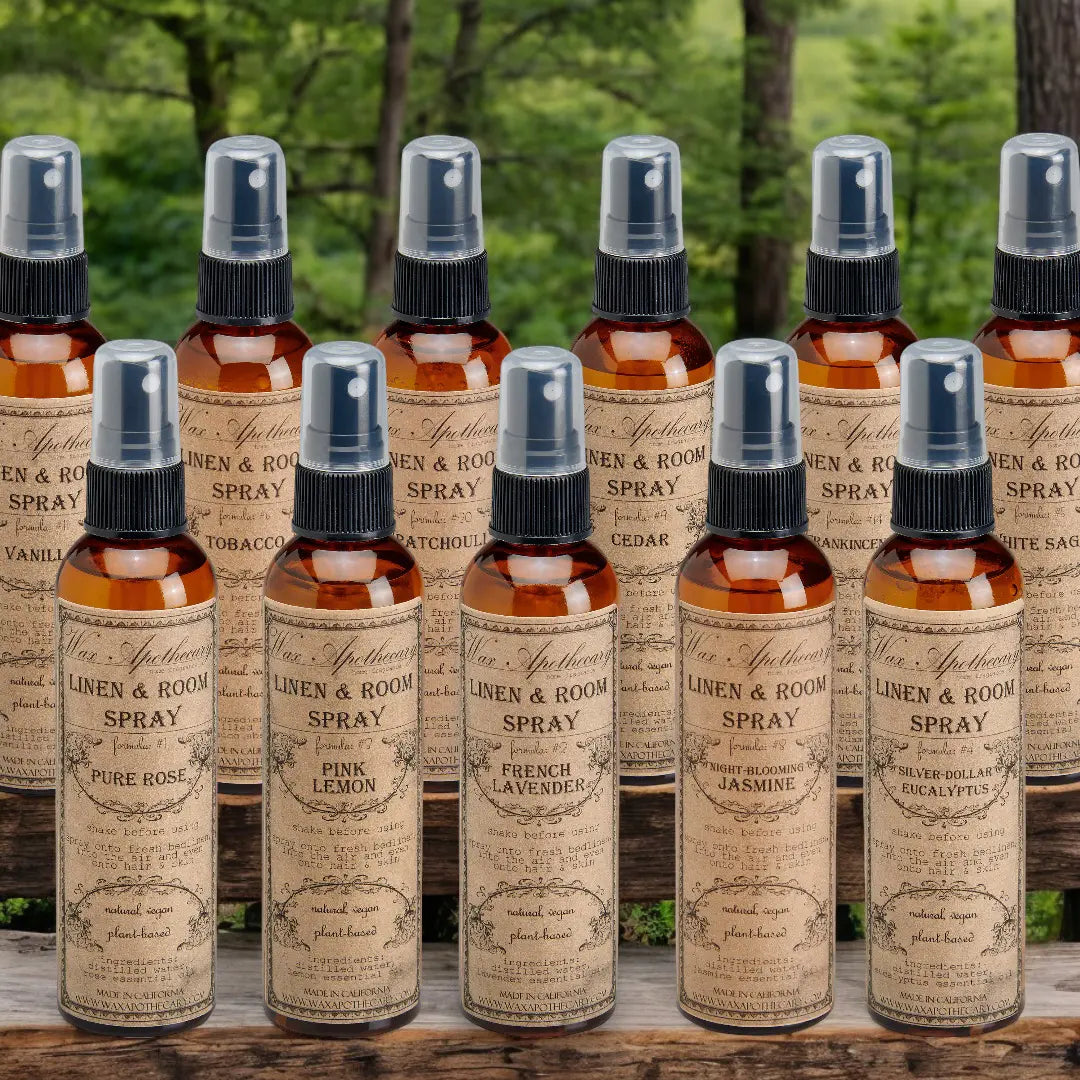 eleven room spray bottles, amber in color with black spray tops sitting on rustic boards in rows with a forest landscape in the background 