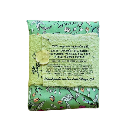 A folded bar of handmade soap in a mint green floral patterned wrapper, tied with a matching lace ribbon and a wooden bead, on a plain white background.
