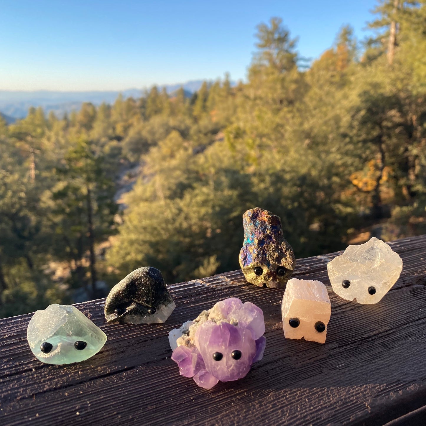 An assortment of rough gemstones with hand carved faces and black bead eyes.  Wax Apothecary